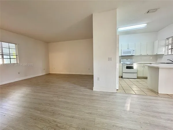 an empty room with wooden floor kitchen appliances and windows