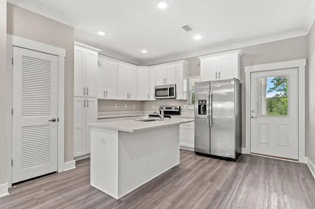 a kitchen with stainless steel appliances granite countertop a refrigerator a sink a stove and white cabinets with wooden floor