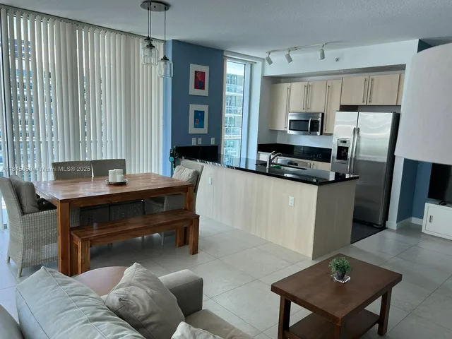 a living room with stainless steel appliances furniture a couch and a kitchen view