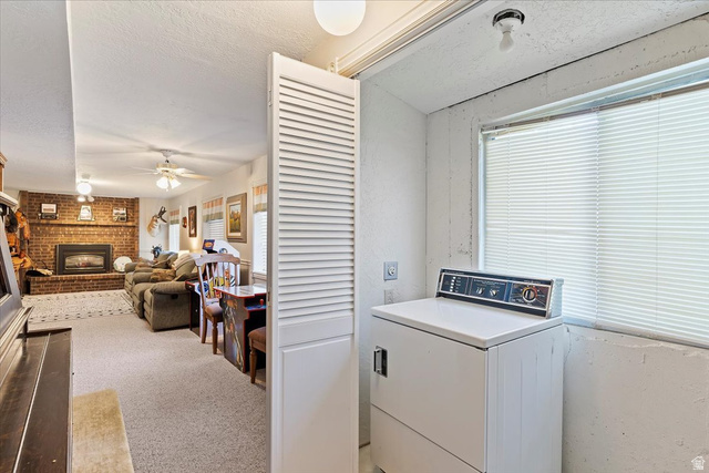 5321 South 3100th Street West Roy, UT 84067 - Photo 37 of 64 Dedicated laundry area with a large window and louvered bifold door, offering direct access to a carpeted living space featuring a brick fireplace with an insert and ceiling fans