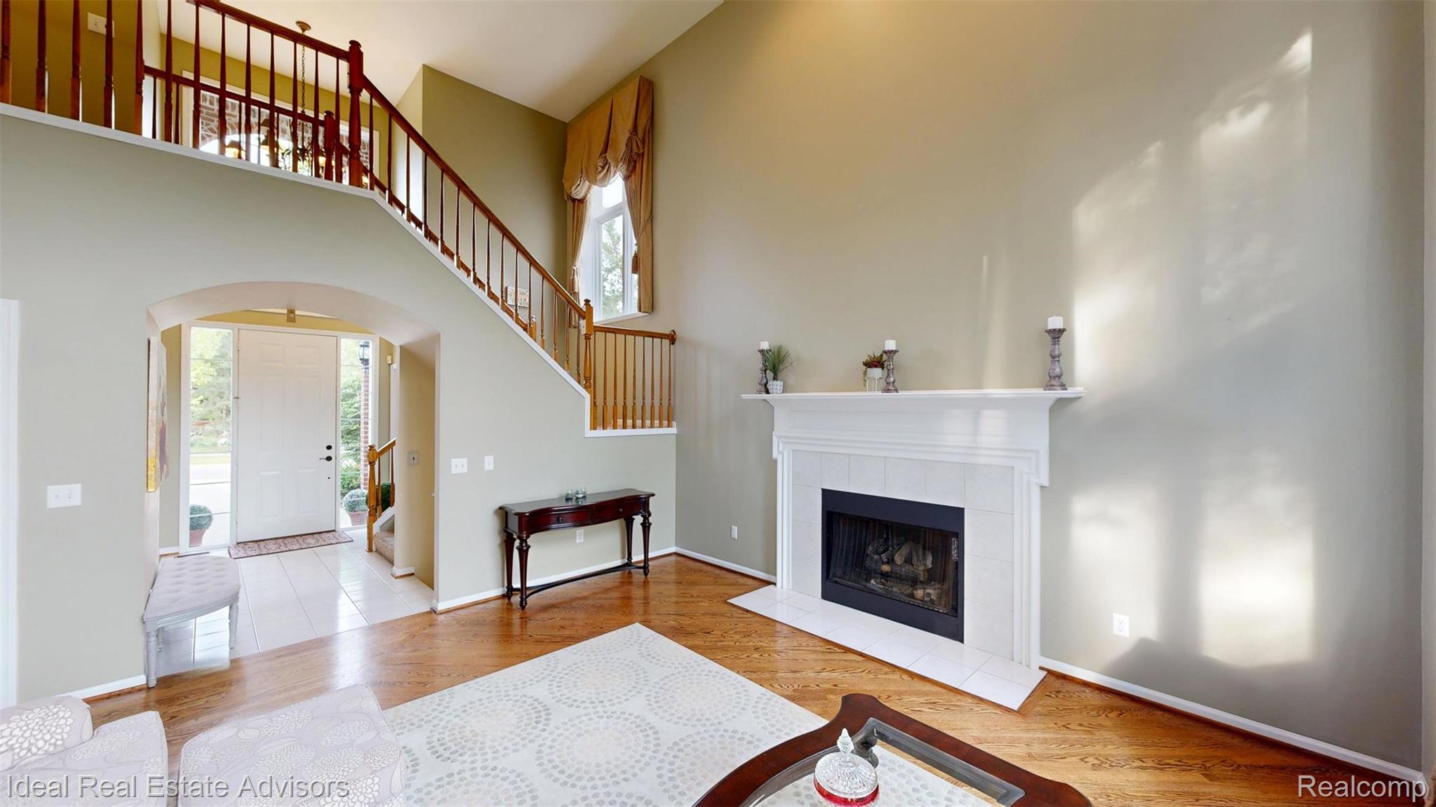 1364 Kentfield Drive Rochester, MI 48307 - Photo 26 of 70 Two-story entry foyer featuring wood-finish flooring, a white mantel fireplace with a tile surround, a grand staircase with wood railings, an arched entryway, and tall windows with custom window treatments