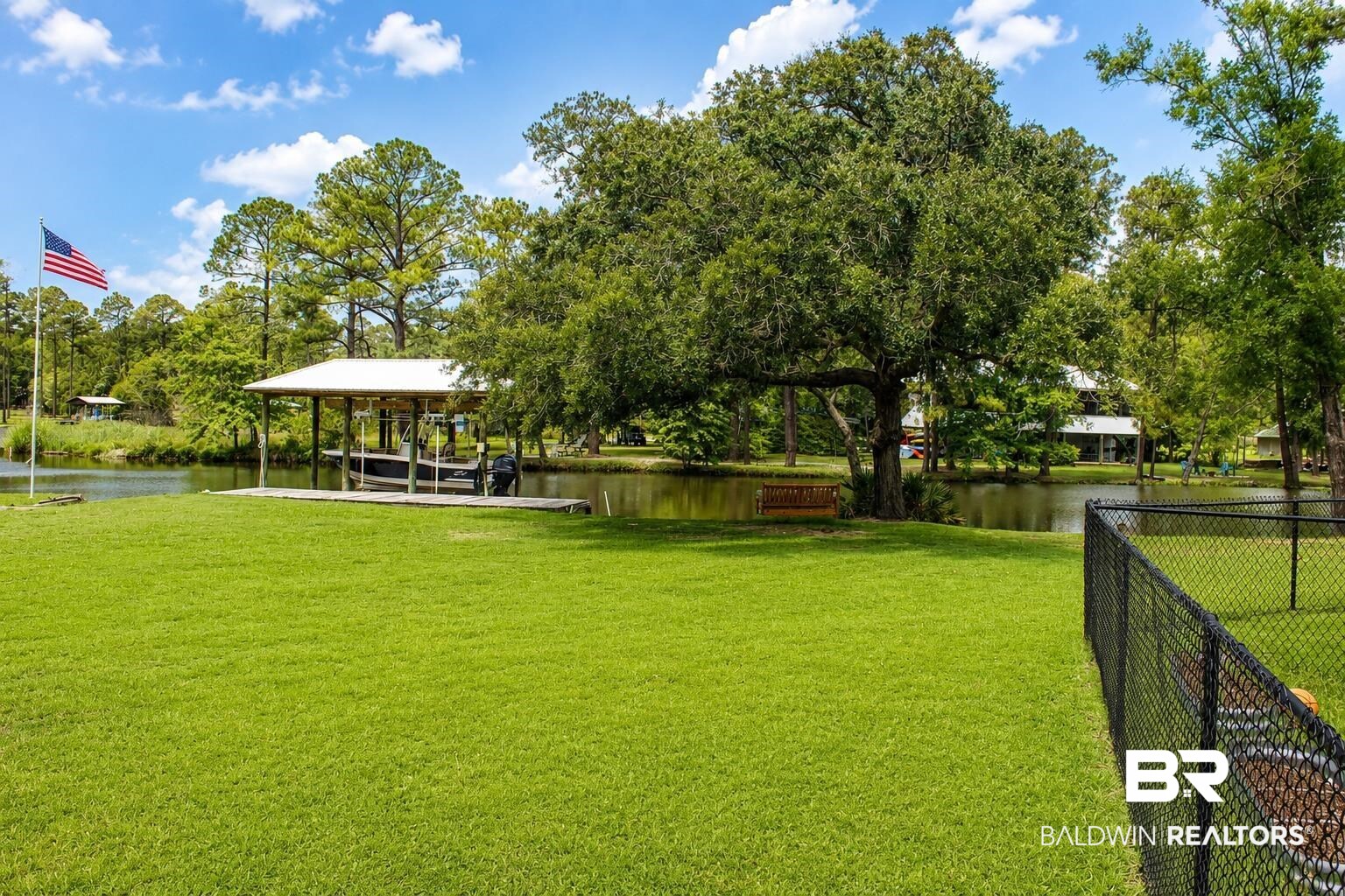 9825 Wolf Creek Ridge Elberta, AL 36530 - Photo 62 of 76 Waterfront property featuring a private boat dock with covered slip, expansive green lawn, mature trees, and secure perimeter fencing