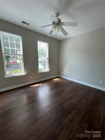 an empty room with wooden floor chandelier fan and windows