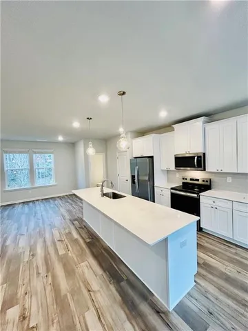 a large kitchen with kitchen island granite countertop a stove a sink a refrigerator and white cabinets with wooden floor