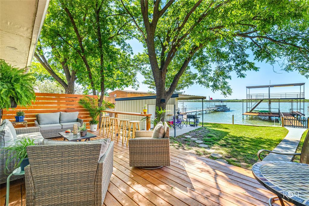 Wooden deck, a boat dock, a water view, outdoor lounge area, and a lawn