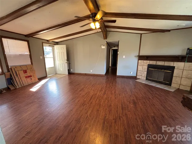 a view of an empty room with wooden floor fireplace and a window