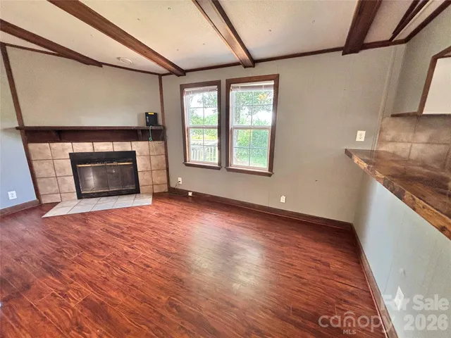 an empty room with wooden floor fireplace and windows