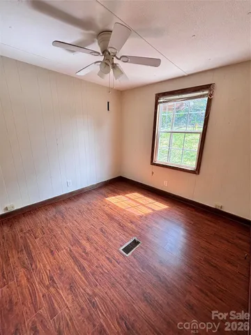 an empty room with wooden floor chandelier fan and windows