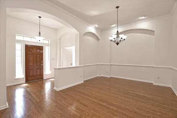 a view of an empty room with wooden floor and a chandelier