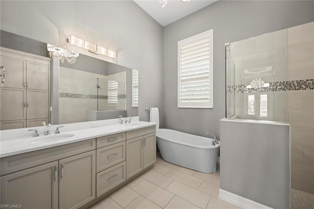 14792 Spinnaker Way Naples, FL 34114 - Photo 19 of 48 a bathroom with a double vanity sink a large mirror and bathtub