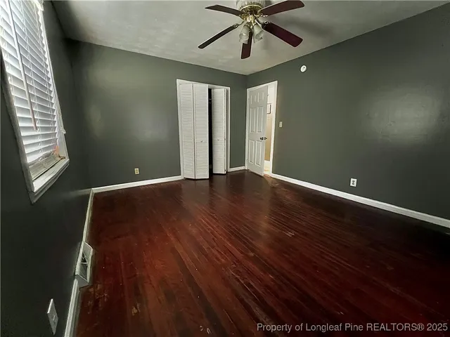 an empty room with wooden floor fan and windows