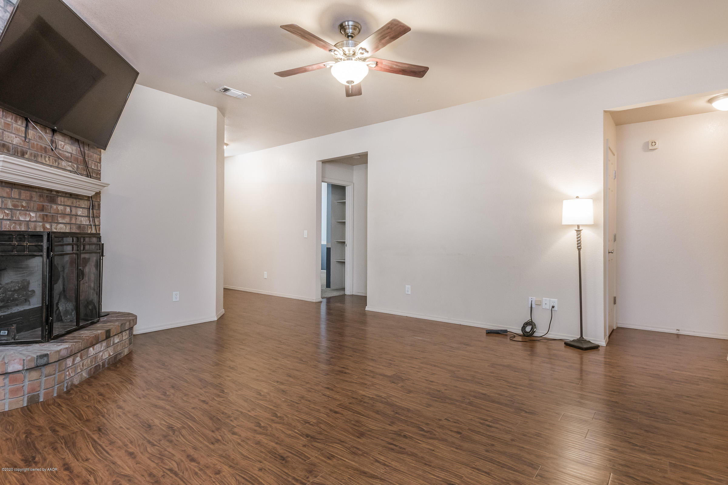 4812 Capulin Lane Amarillo, TX 79110 - Photo 3 of 20 an empty room with wooden floor a flat screen tv and a fireplace