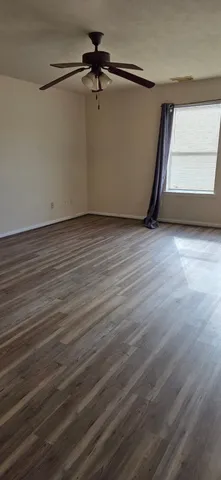 an empty room with wooden floor fan and windows