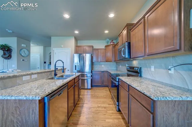 a kitchen with stainless steel appliances granite countertop a sink a stove and a wooden cabinets