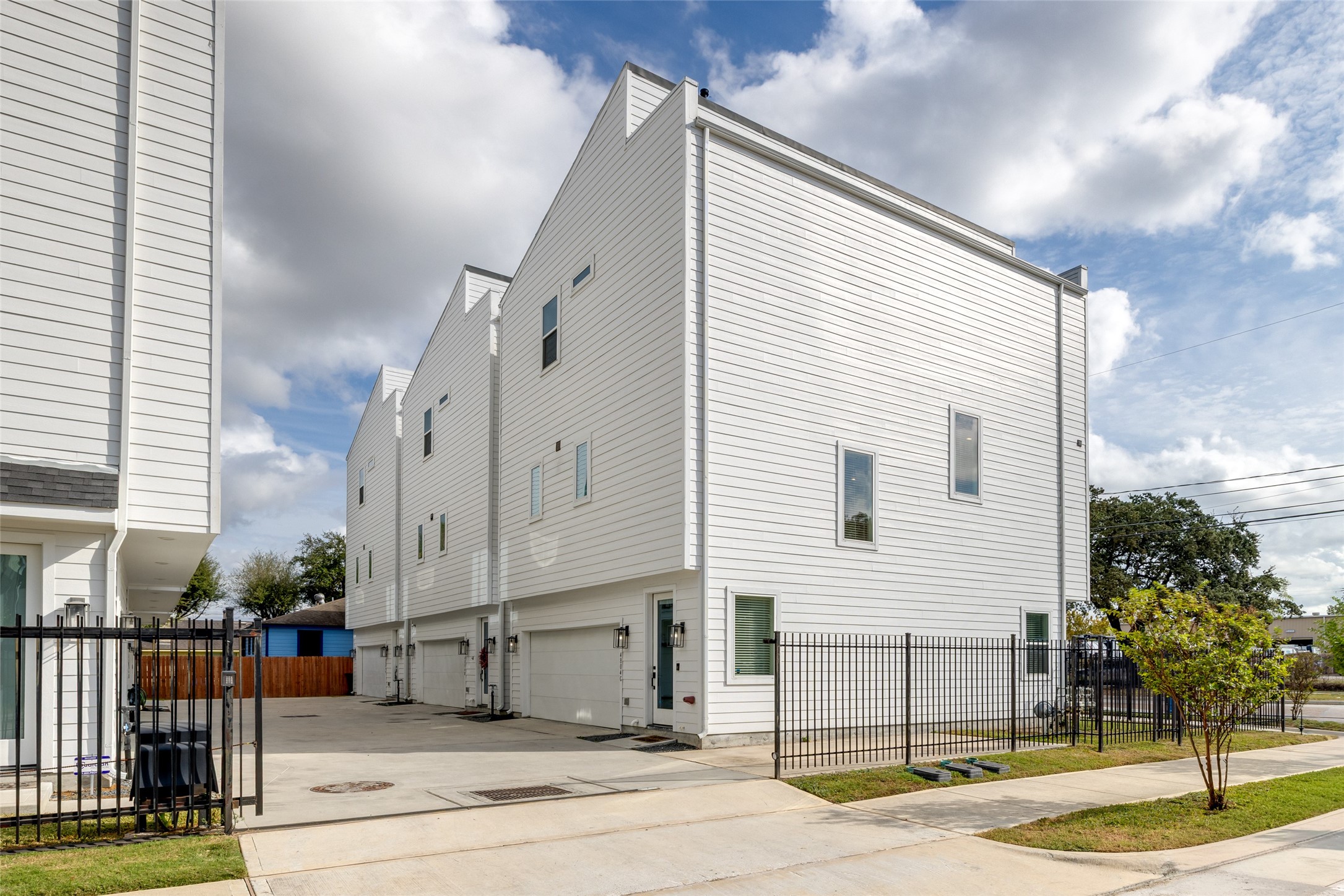Modern townhome with a sleek white exterior, featuring clean lines and large windows. It has a fenced driveway and garage, providing a secure and private entrance. Perfect for contemporary living.