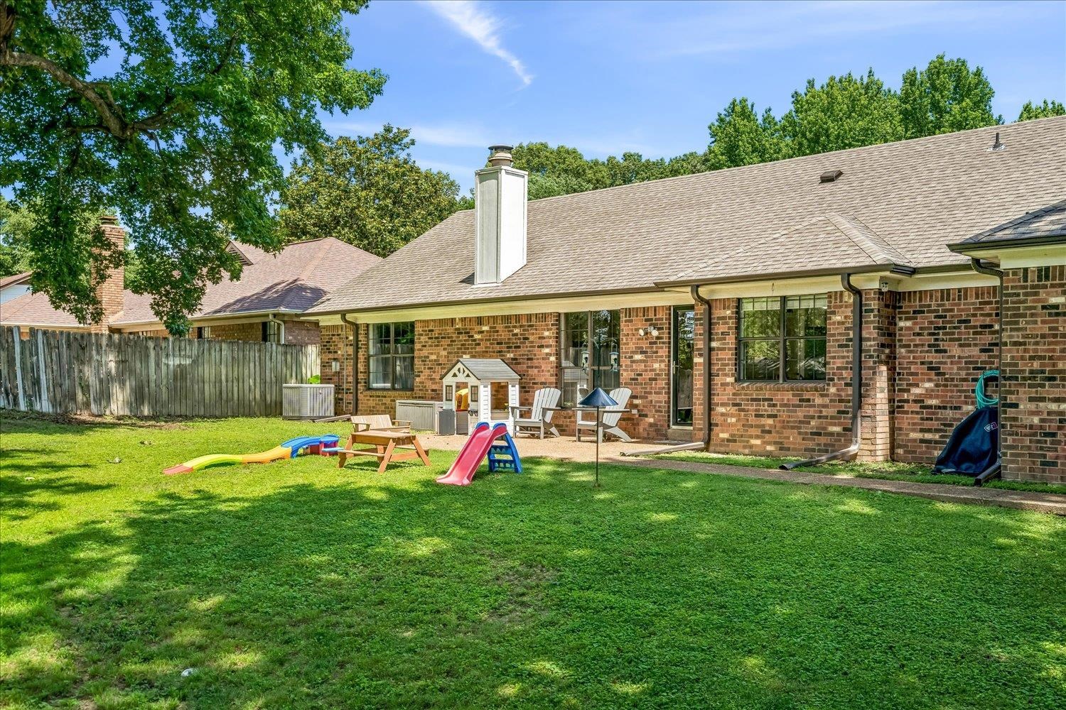 5711 Yale Road Bartlett, TN 38134 - Photo 28 of 29 Spacious rear yard featuring a large patio, brick exterior, multiple windows, and a mature tree providing shade