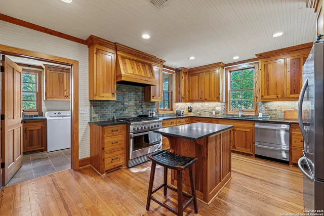 a kitchen with stainless steel appliances granite countertop wooden cabinets a sink a stove a refrigerator and dishwasher with wooden floor