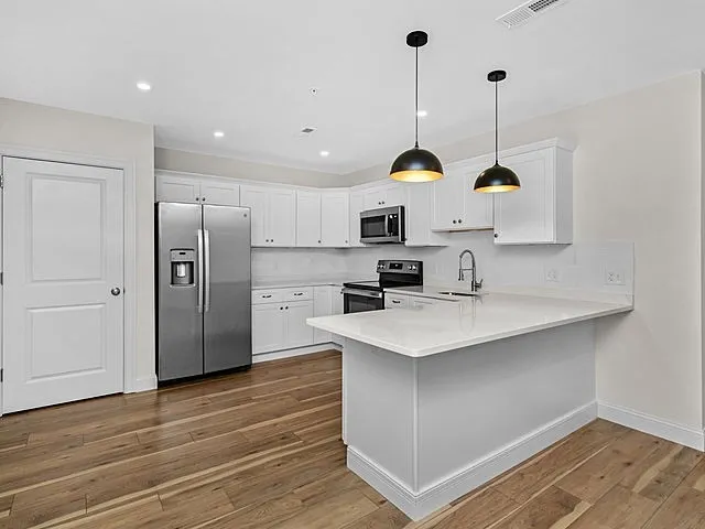 a kitchen with stainless steel appliances granite countertop a sink a stove a refrigerator and island with wooden floor