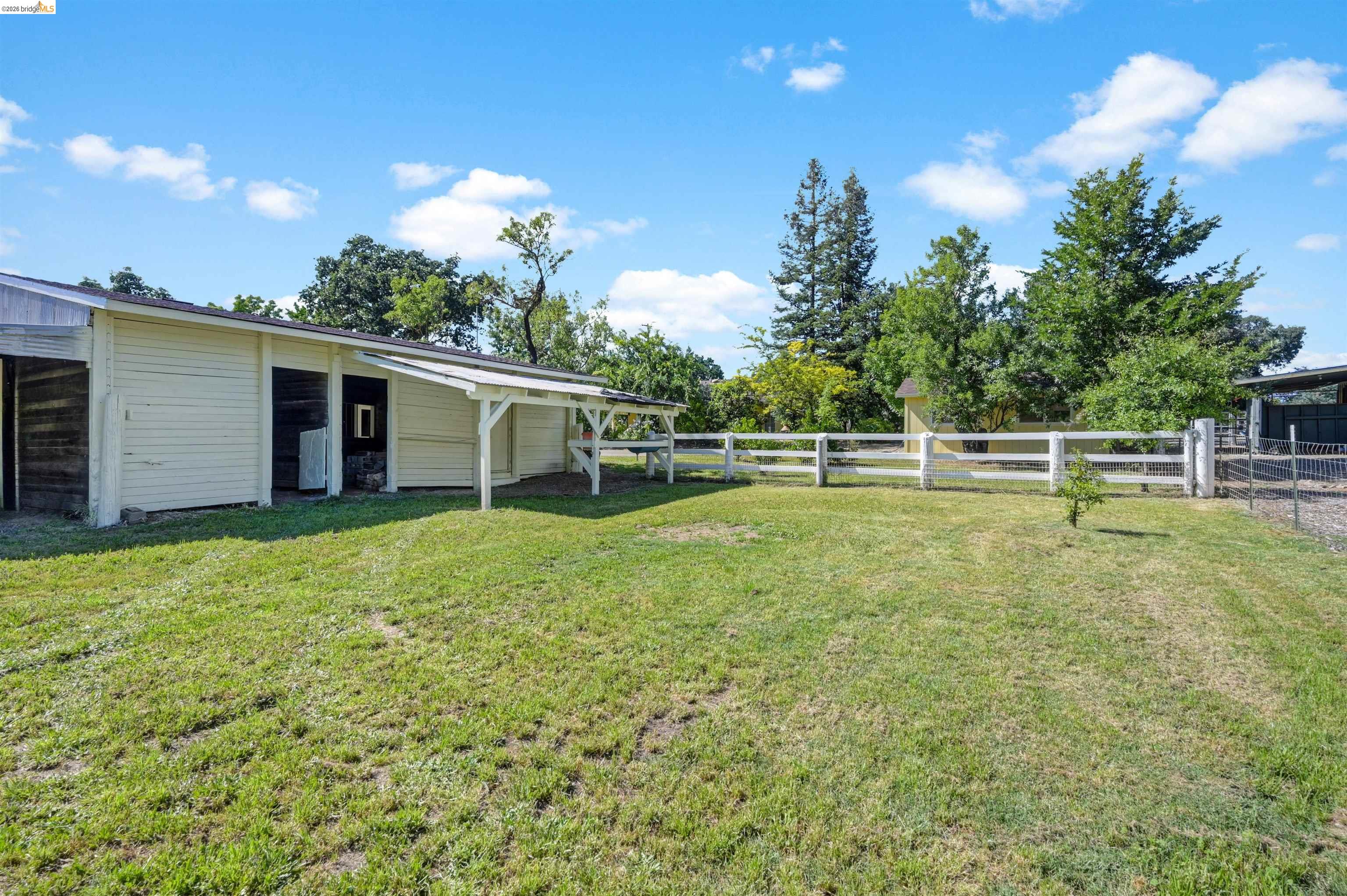 10474 Sheldon Road Elk Grove, CA 95624 - Photo 61 of 83 Expansive outdoor space featuring a barn structure with an extended overhang, white split-rail fencing, and mature trees