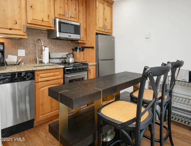 a kitchen with stainless steel appliances granite countertop a stove a refrigerator a microwave a dining table and chairs with wooden floor