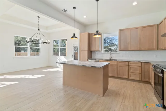 a kitchen with stainless steel appliances granite countertop a sink a stove a refrigerator and island with wooden floor