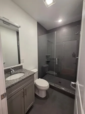 a bathroom with a granite countertop sink a toilet a mirror and shower