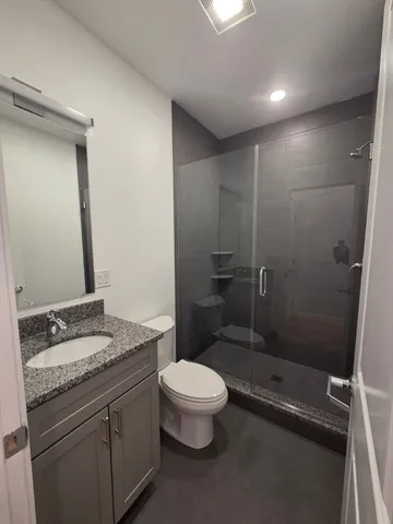 a bathroom with a granite countertop sink a toilet a mirror and shower