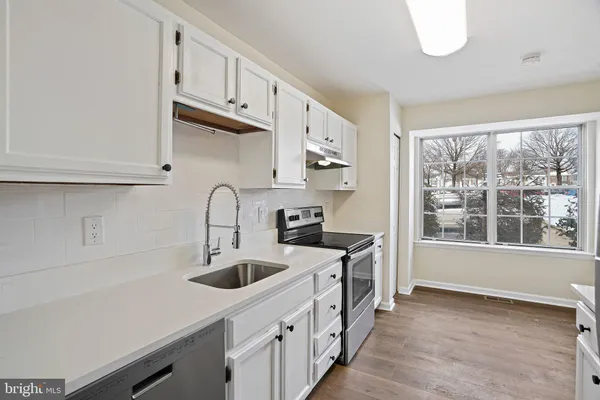 a kitchen with stainless steel appliances sink a stove and white cabinets with wooden floor