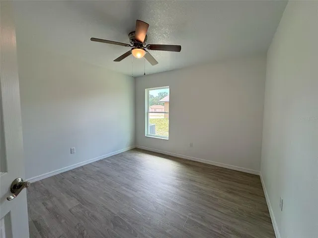 an empty room with wooden floor chandelier fan and windows