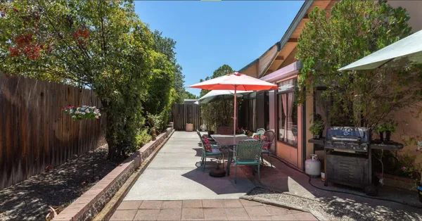a view of a patio with a table and chairs under an umbrella with a barbeque