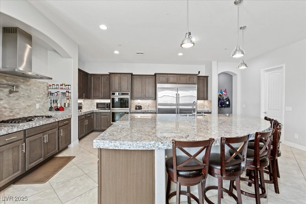 259 Milan Street Henderson, NV 89015 - Photo 22 of 99 Kitchen with decorative backsplash, light tile patterned flooring, dark brown cabinetry, arched walkways, and wall chimney exhaust hood