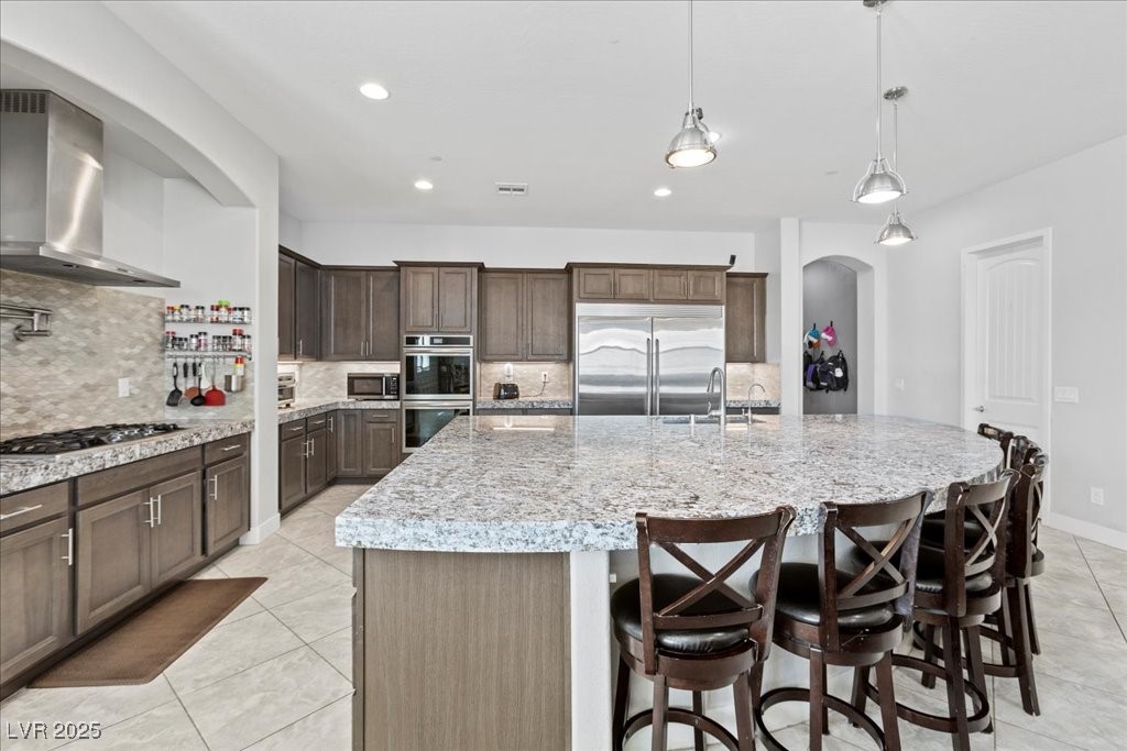 259 Milan Street Henderson, NV 89015 - Photo 23 of 99 Kitchen featuring tasteful backsplash, wall chimney exhaust hood, recessed lighting, arched walkways, and dark brown cabinets