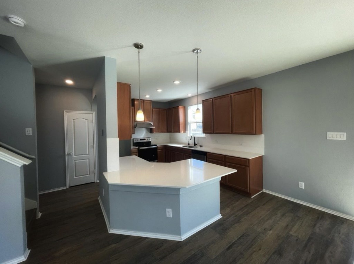 13905 Inaugural Street Manor, TX 78653 - Photo 5 of 26 Kitchen featuring light countertops, stainless steel appliances, decorative light fixtures, a peninsula, and dark wood-style floors