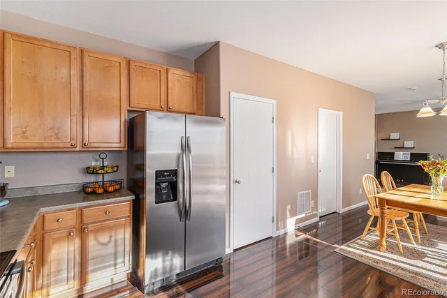 a kitchen with stainless steel appliances granite countertop a refrigerator a stove a sink a dining table and chairs with wooden floor