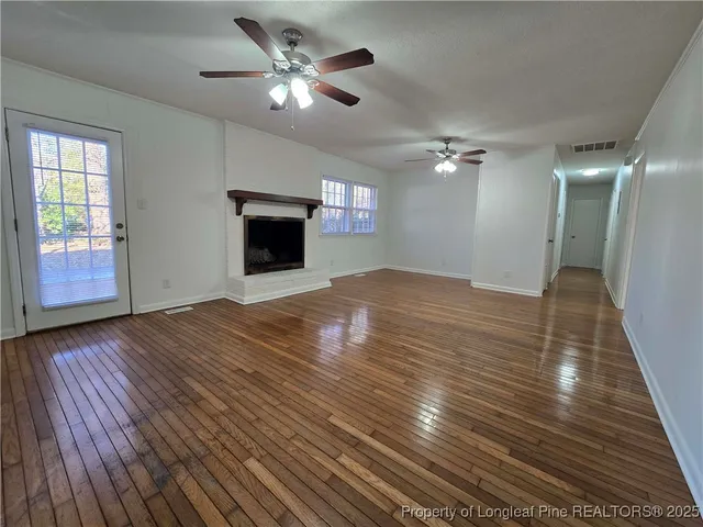 a view of an empty room with wooden floor and a ceiling fan