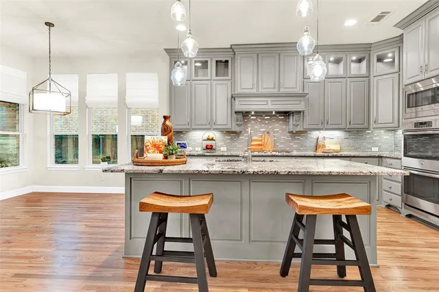 a kitchen with stainless steel appliances granite countertop a table chairs sink and cabinets with wooden floor