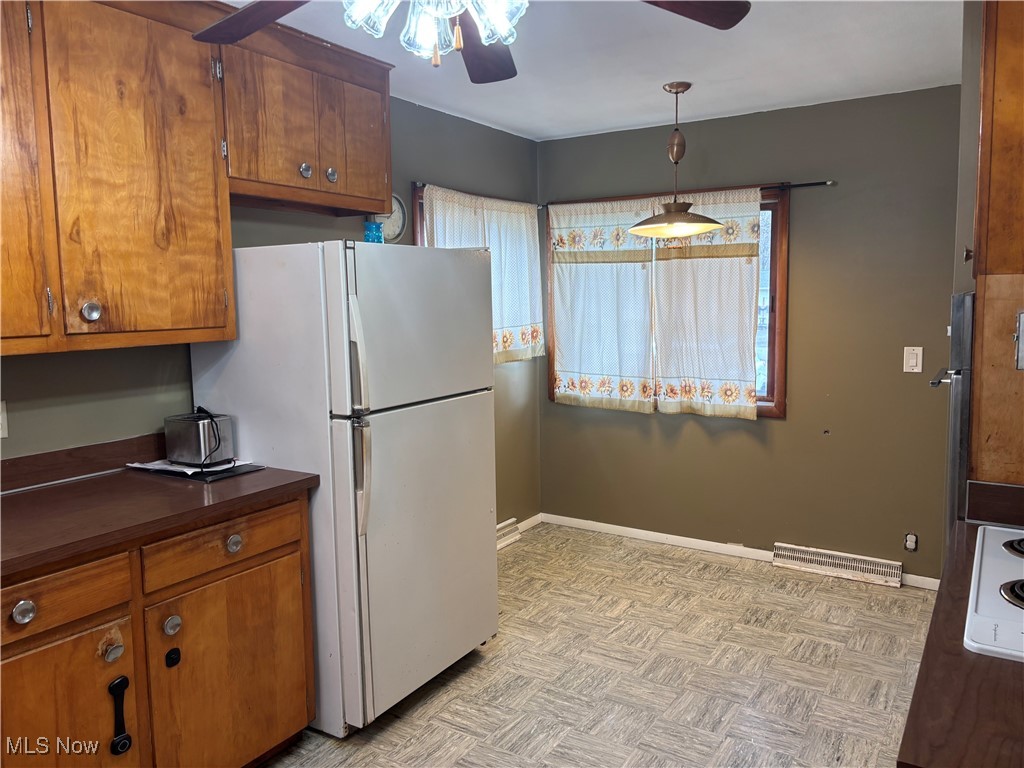 Kitchen featuring freestanding refrigerator, a ceiling fan, dark countertops, and brown cabinets