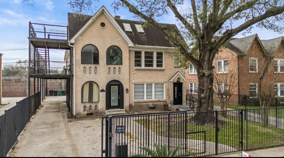 a view of a white house with a large tree and wooden fence