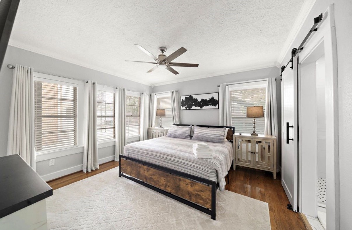 1633 Castle Court Houston, TX 77006 - Photo 11 of 38 Staged primary bedroom featuring abundant natural light, warm hardwood floors, and a spacious layout. The room showcases a modern ceiling fan, neutral tones, and elegant décor, creating a calm and inviting retreat with ample space for relaxation and comfort.