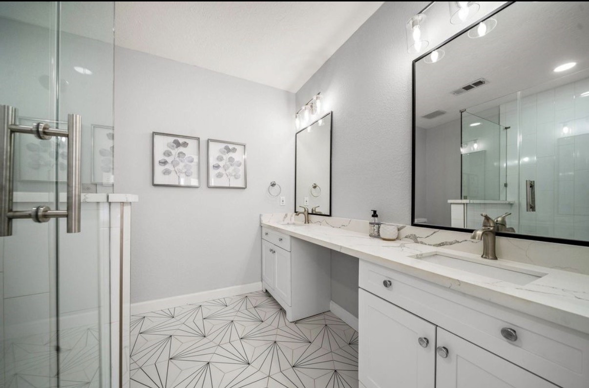 1633 Castle Court Houston, TX 77006 - Photo 17 of 38 Staged spa-like primary bathroom featuring a large glass-enclosed shower, dual sinks with modern fixtures, expansive counter space, and stylish framed mirrors. Soft gray tones, updated lighting, and elegant flooring create a bright, calming retreat with plenty of room for daily comfort and convenience.