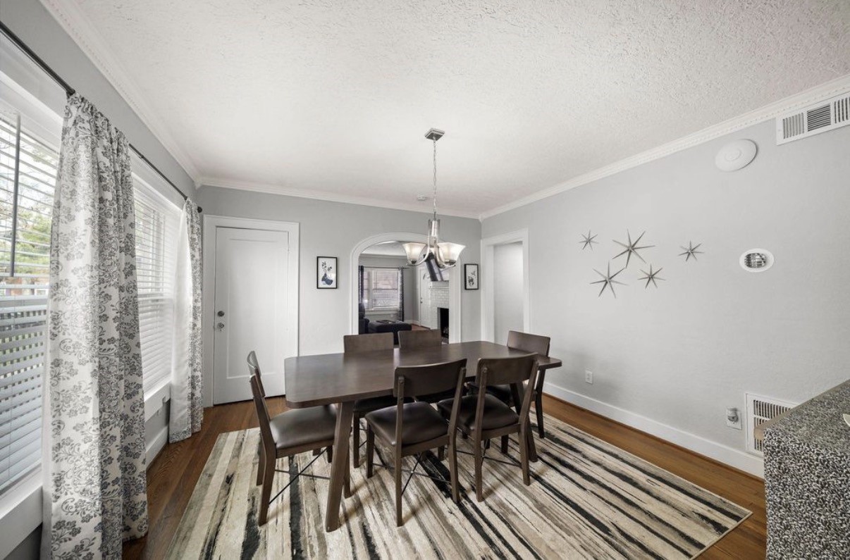 1633 Castle Court Houston, TX 77006 - Photo 5 of 38 Staged dining room showcasing bright natural light, timeless hardwood floors, and a spacious layout perfect for gatherings. The curated furnishings highlight how comfortably the space can accommodate large dining setups while maintaining an elegant, inviting atmosphere.