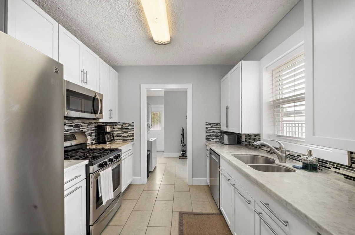 1633 Castle Court Houston, TX 77006 - Photo 6 of 38 Bright and updated kitchen featuring sleek white cabinetry, stainless steel appliances, and a stylish mosaic tile backsplash. The galley layout offers ample counter space, a double sink, and great natural light from the window. Conveniently leads into the laundry area for added functionality.