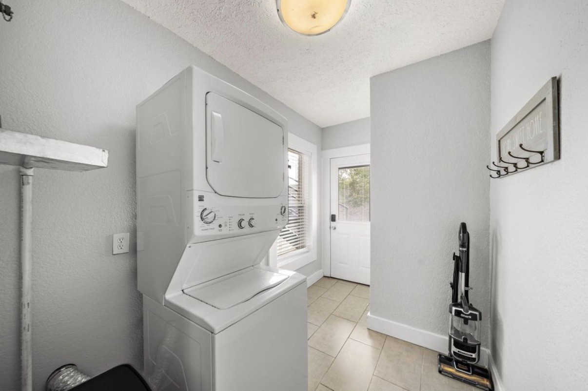 1633 Castle Court Houston, TX 77006 - Photo 8 of 38 Staged laundry area featuring a stacked washer and dryer, bright natural light, and updated finishes. This spacious utility room offers added convenience with extra storage options, modern tile flooring, and easy access to adjoining areas—making everyday chores feel more organized and efficient.