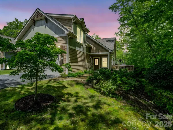 a yellow house with a small yard plants and large trees