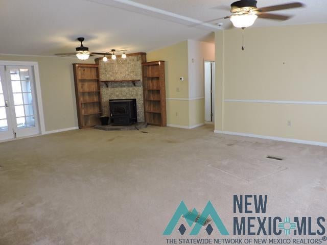 35 Mays Road Clayton, NM 88415 - Photo 15 of 31 Spacious interior featuring a built-in fireplace with a stone surround, integrated wood-finish shelving, and twin ceiling fans