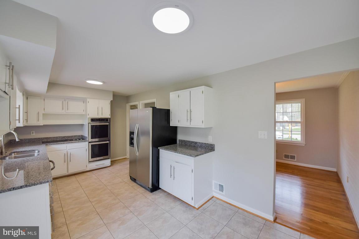 6716 Huntsman Boulevard Springfield, VA 22152 - Photo 3 of 30 a kitchen with stainless steel appliances kitchen island granite countertop a refrigerator oven a sink with white cabinets and wooden floor