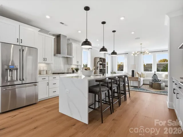 a kitchen with stainless steel appliances kitchen island granite countertop a stove a refrigerator a oven and a dining table with wooden floor