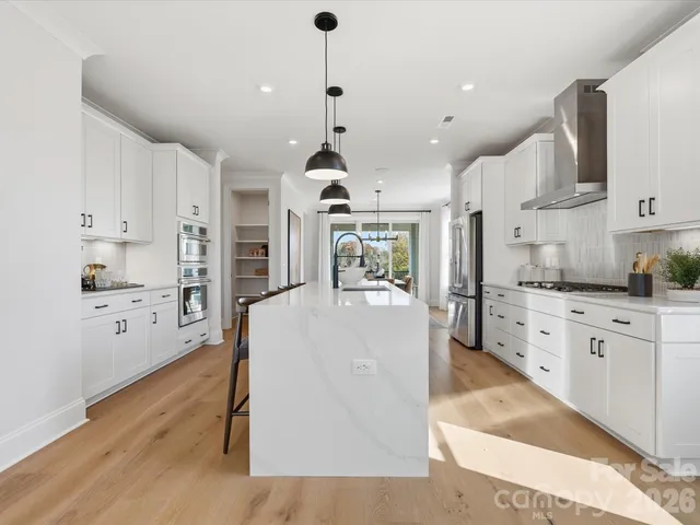 a large kitchen with kitchen island a stove a sink a refrigerator and white cabinets with wooden floor