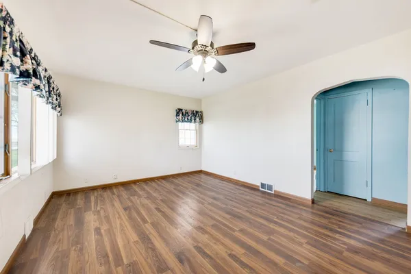 an empty room with wooden floor chandelier fan and windows