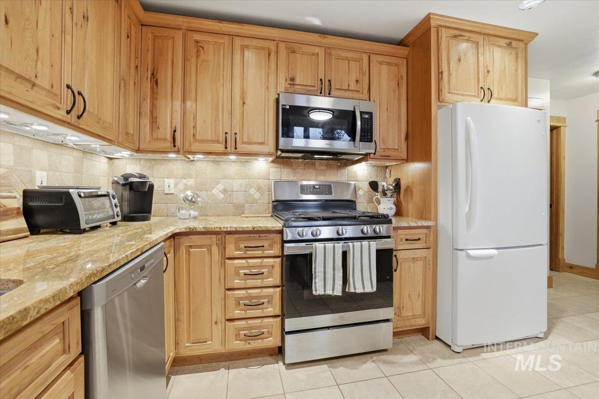 20 Valley High Road Garden Valley, ID 83622 - Photo 16 of 46 Kitchen with appliances with stainless steel finishes, light stone counters, tasteful backsplash, and light tile patterned floors